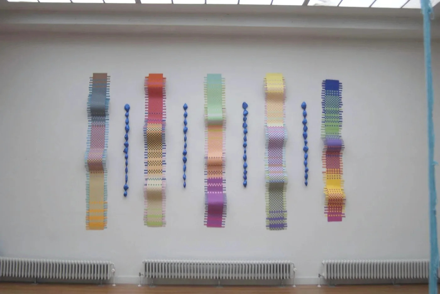 Flow, colourful woven forms and blue suspended elements in an exhibition space