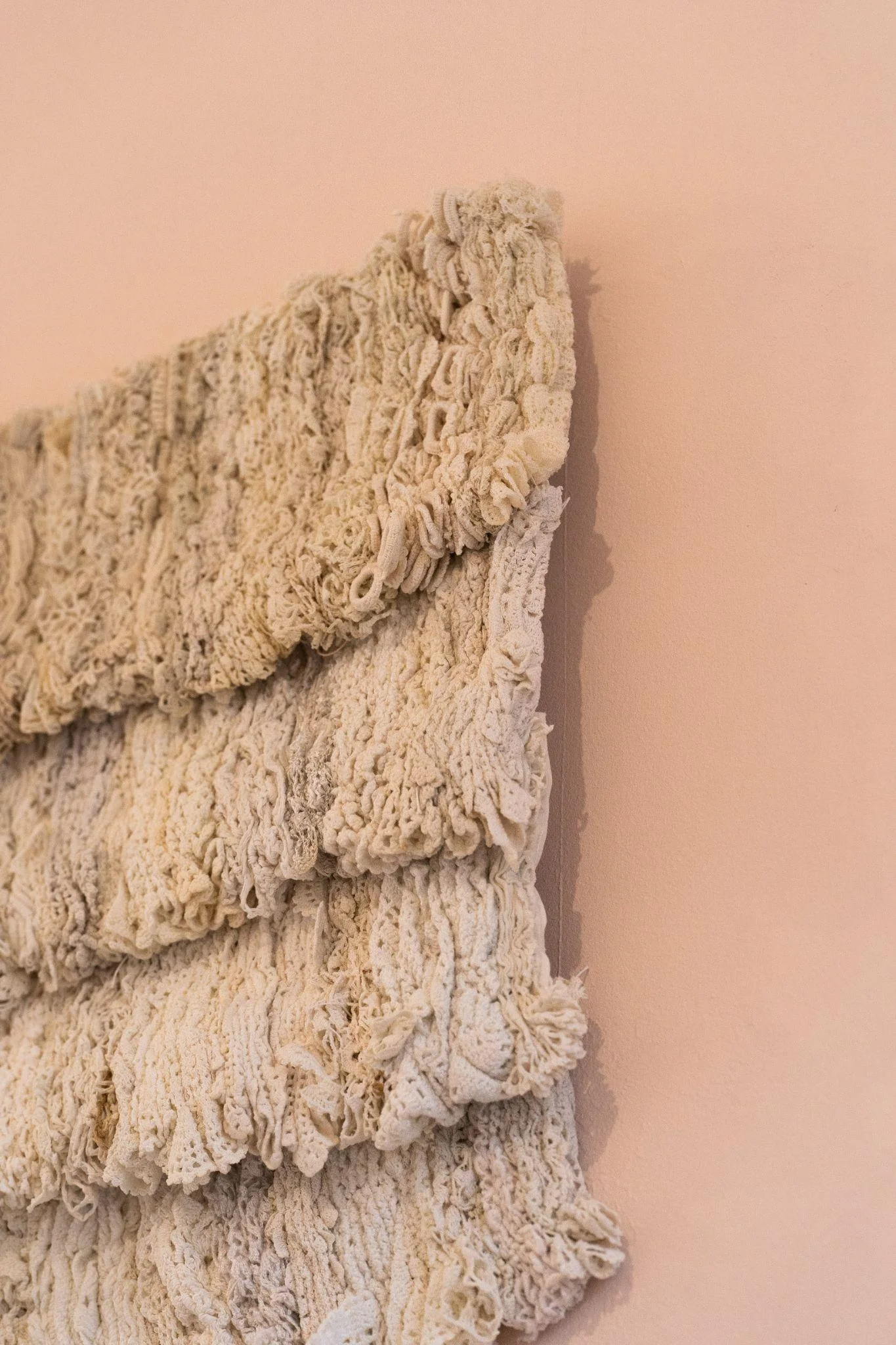 Layered textile hanging against a warm-coloured wall