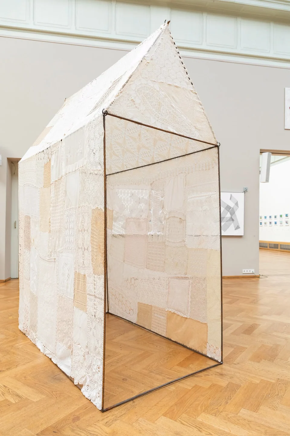 House-shaped lace installation on a metal frame in a gallery