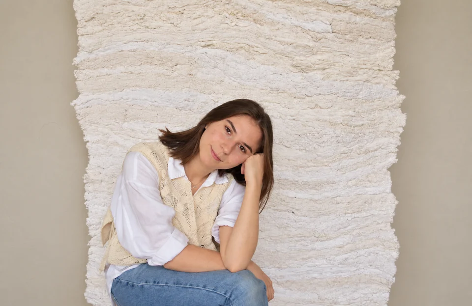 Hara Athanasopoulou seated in front of her textile artwork